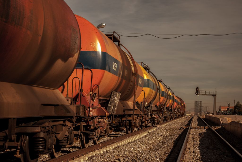 A long freight train with hazardous materials tank cars on a railway track under a bright sky.