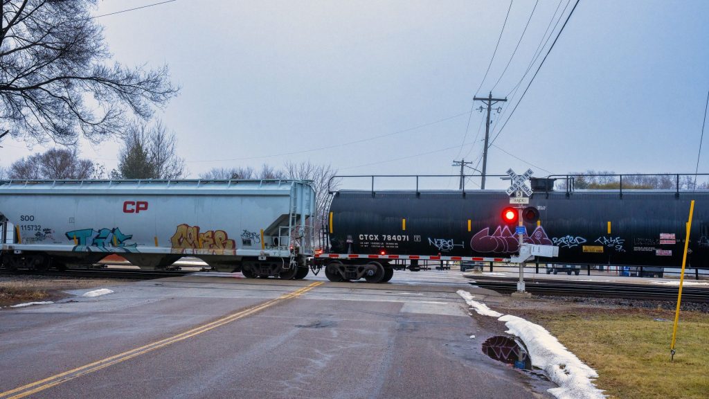 Freight train crossing a rural road in Wabasha, Minnesota during winter with visible graffiti.